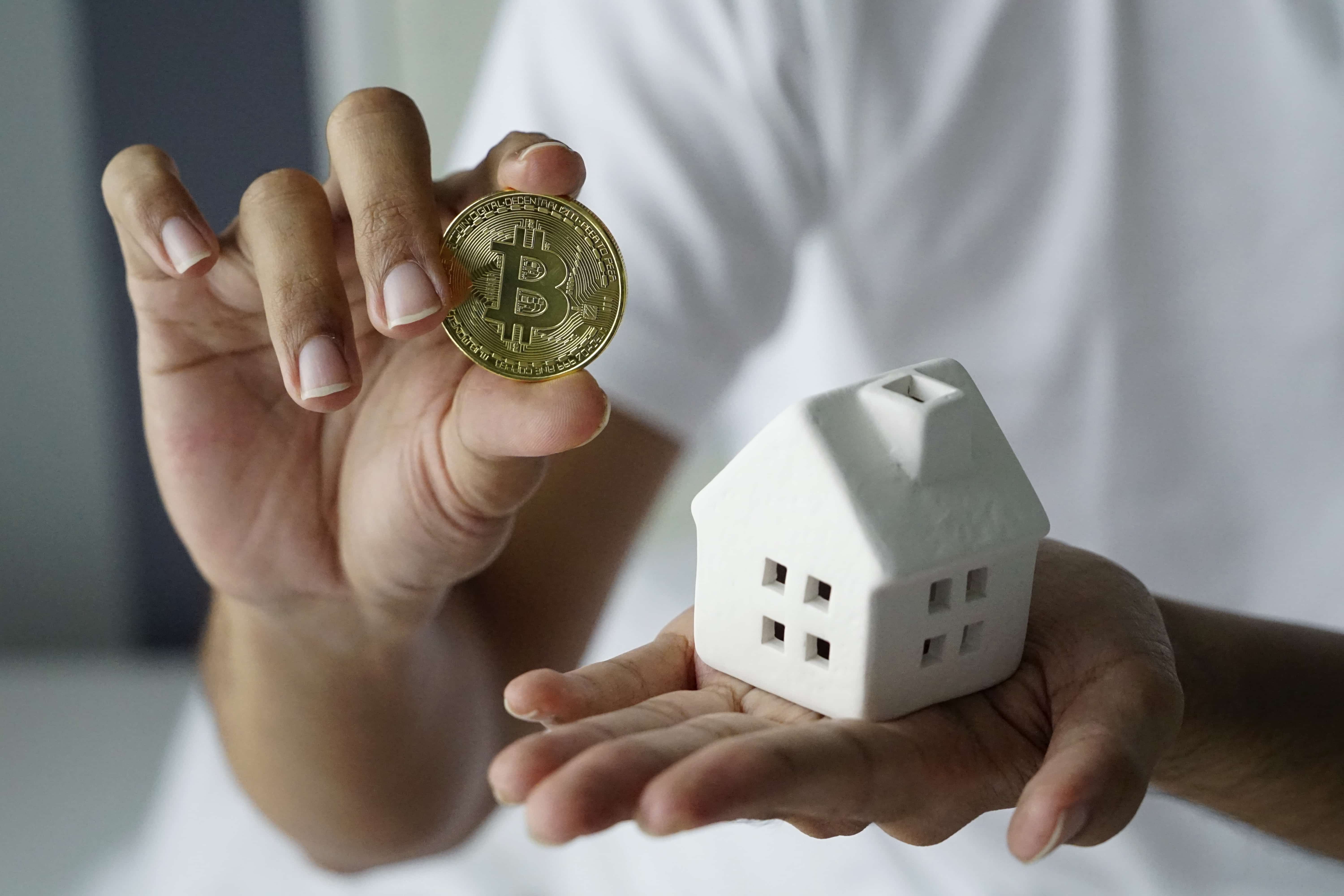 Close up, Young man holding bitcoin and with home in hand. Man saving money for new home. Business man hand holding a money bit coin and a model home.Male holding Model house Home Loans with money
